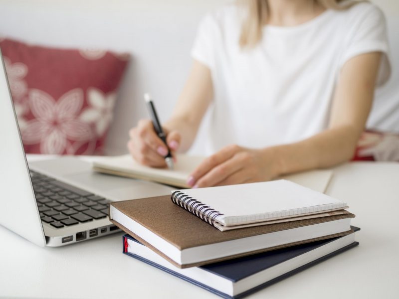 imagen ilustrativa que muestra una persona escribiendo junto a libros y una computadora portatil